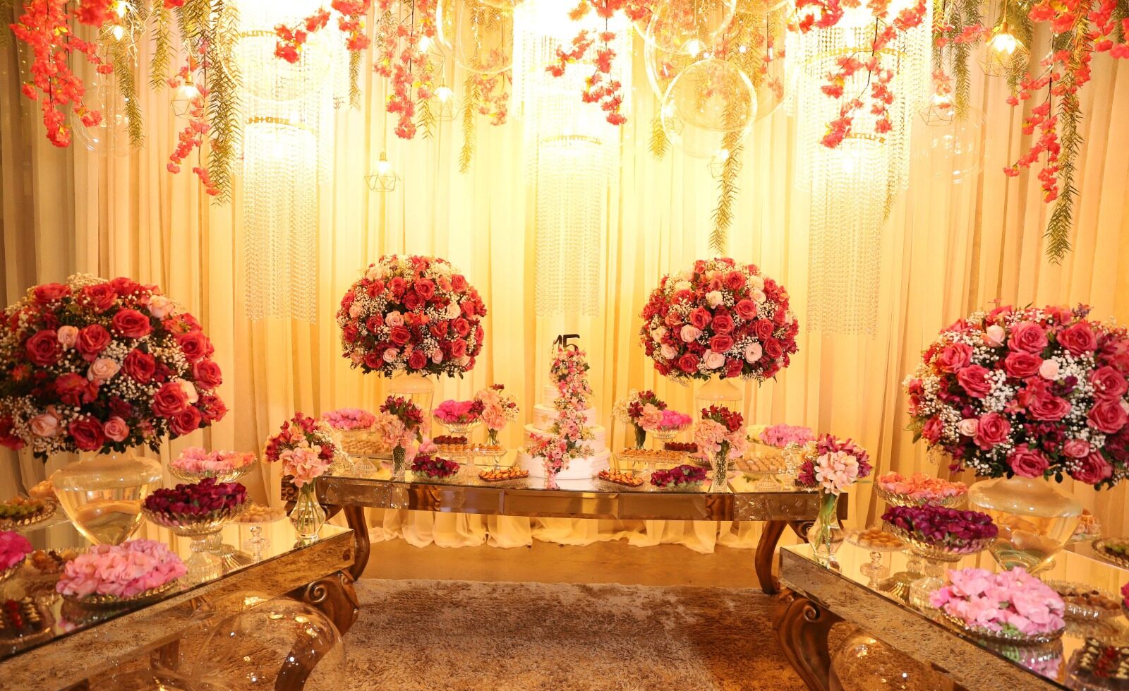 Mesa de doces com arranjos de rosas e teto de flores